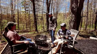 a group of people sitting around a fire in the woods at Luxurious Safari Tent in Cooperstown, NY - Perfect Glamping Spot for a Romantic Getaway in Cooperstown