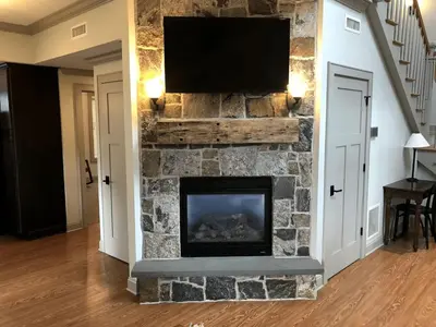 a living room with a stone fireplace with a flat screen tv at Beautiful Cottage Rental on Lakeside Property in Berkshires, Massachusetts in Lanesborough