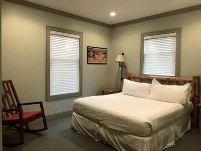 a bedroom with a bed and a chair and two windows at Beautiful Cottage Rental on Lakeside Property in Berkshires, Massachusetts in Lanesborough