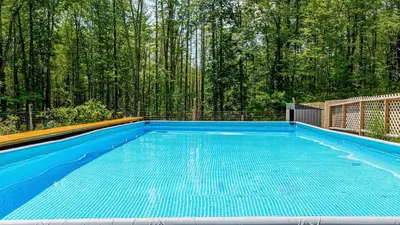 a blue swimming pool with trees in the background at PoolHot Tub Firepit Near Hikes Shops Dining Cragswood Lodge by AvantStay in New Paltz