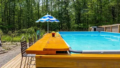 a wooden table with an umbrella next to a swimming pool at PoolHot Tub Firepit Near Hikes Shops Dining Cragswood Lodge by AvantStay in New Paltz