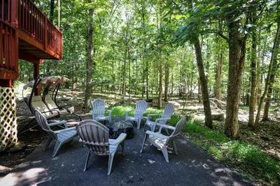 a patio with a table and chairs in the woods at Mahogany Sun Hot Tub Theater Room Fire Pit in East Stroudsburg