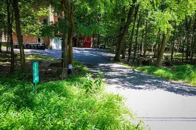 a tree lined road with a sign in the grass at Twin Pines Retreat Hot Tub Theater Room Fire in East Stroudsburg