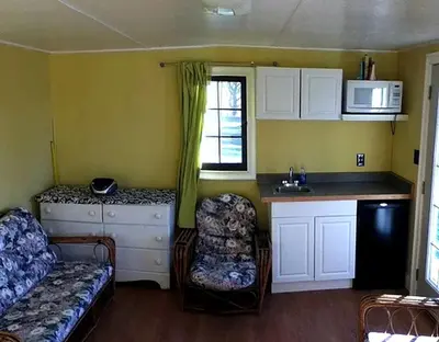 a living room with a couch and a kitchen with a sink at Comfortable Cabin Right on Great Sacandaga Lake in Northville, New York in Northville