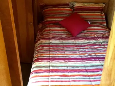 a small bed with a red pillow on it at Rustic Cabin Beside the Great Sacandaga Lake in Northville, New York in Northville