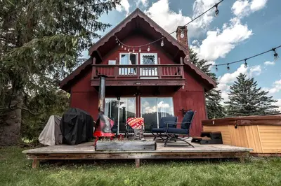 a red cabin with a deck and a chair in front at Rustic Cabin Rental with a Hot Tub near Windham, New York in Windham