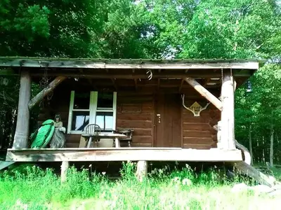 a small log cabin with a porch and a chair at Pet-Friendly Rustic Cabin on Grafton Mountain, New York in Johnsonville