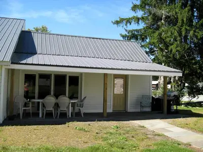 a white house with a porch with a table and chairs at Unique Renovated Barn Rental with Pond near Cooperstown, New York in Fly Creek