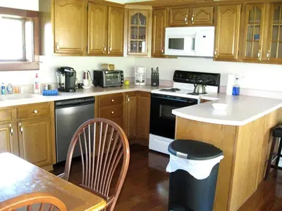 a kitchen with wooden cabinets and a black and white appliance at Unique Renovated Barn Rental with Pond near Cooperstown, New York in Fly Creek