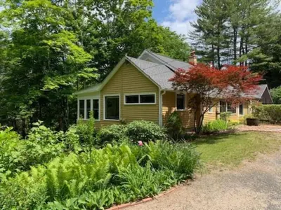 a yellow house with a garden in front of it at Luxurious Riverfront Cottage with a Hot Tub and a Fireplace near the Twin Lakes, Connecticut in Canaan