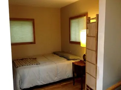 a bedroom with a bed and a table and two windows at Romantic Mountain Cabin with Stunning Views in Ulster County, New York in Shandaken