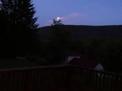 a moonrise over a hill with a house and trees at Romantic Mountain Cabin with Stunning Views in Ulster County, New York in Shandaken