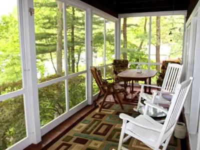 a screened in porch with white chairs and a table at Delightful Vacation Rental with a Private Dock on Candlewood Lake in Connecticut in New Milford