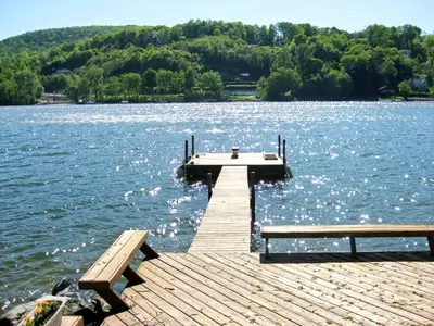 a wooden dock with two benches on a lake at Delightful Vacation Rental with a Private Dock on Candlewood Lake in Connecticut in New Milford