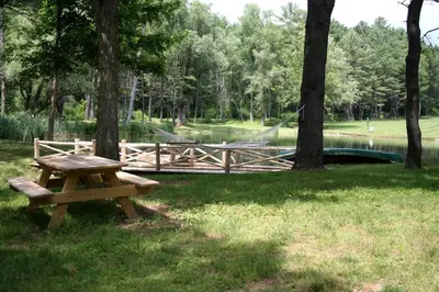 a wooden picnic table sitting in the grass next to a pond at Gorgeous Green Mountains Vacation Rental with a Pool in Manchester, Vermont in Manchester Center