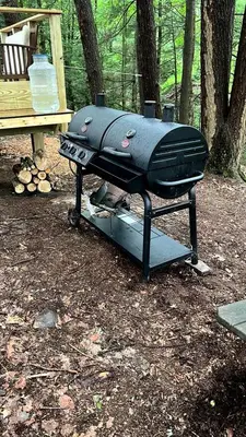 a grill sitting in the woods next to a bench at Amazing Equipped Bell Tent Nestled Among Nature in New York in Kerhonkson