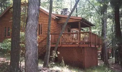 a log cabin with a deck in the woods at Idyllic Waterfront Log Cabin in Wayne County Overlooking Lake Wallenpaupack, Pennsylvania in Lakeville