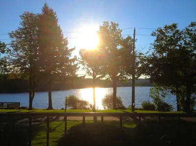 a sun setting over a lake with trees and a fence at Peaceful Private Cabin on Crystal Lake near Elk Mountain, Pennsylvania in Clifford