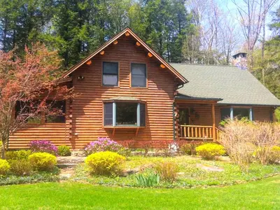 a log cabin with a garden in front of it at Cozy Log Cabin with a Private Hot Tub near Beartown State Forest, Massachusetts in Monterey