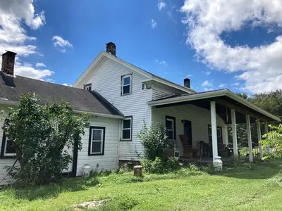a white house with a porch and a yard at Lovely Farmhouse Cabin with Incredible Landscape Views in New York in Worcester