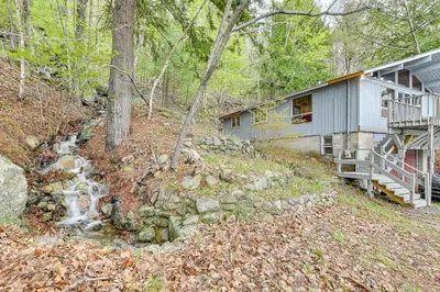 a house in the woods with a creek next to it at Lake-View Cabin with Furnished Deck in Hadley! in Hadley