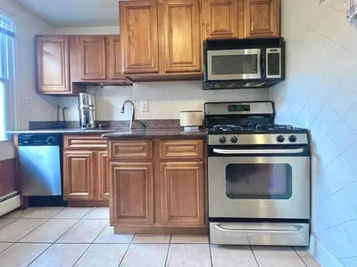 a kitchen with wooden cabinets and a stove and microwave at Ten Minute Commute to NYC in Jersey City