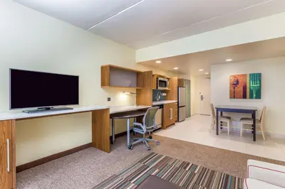 a hotel room with a desk with a tv and a kitchen at Home2 Suites by Hilton Albany Airport/Wolf Rd in Albany