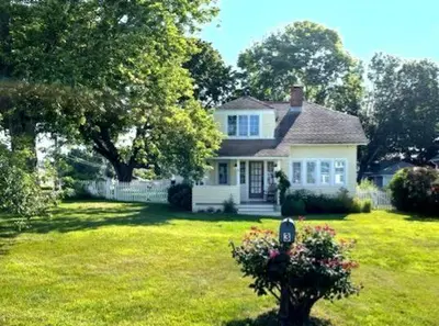 a white house in a yard with a tree at Enchanted Cottage 1 block to beach in Madison