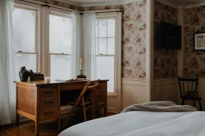 a bedroom with a desk and a bed and windows at Book Village Inn - Twain Room Queen Bed in Hobart