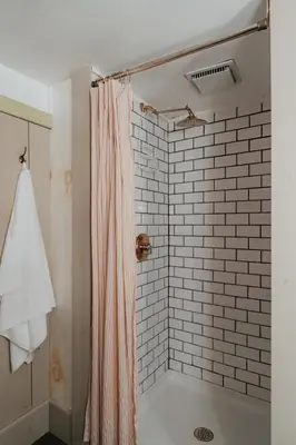 a bathroom with a shower curtain and a tile wall at Book Village Inn - Fitzgerald Room King Bed in Hobart
