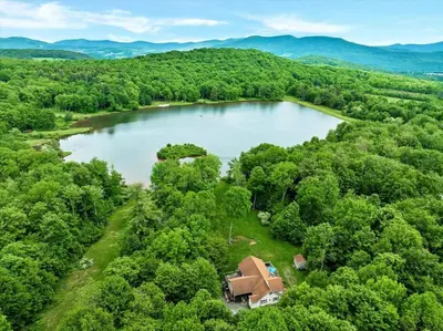 an aerial view of a lake with a house at Wooded lakefront chalet with hot tub and game room in South Kortright