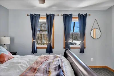 a bedroom with blue curtains and a bed and a window at Wooded lakefront chalet with hot tub and game room in South Kortright