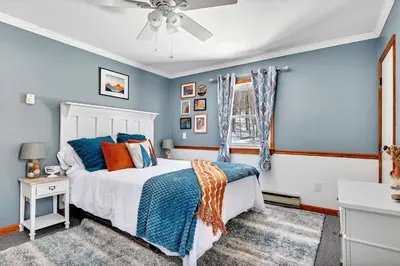 a bedroom with a bed with blue walls and a window at Wooded lakefront chalet with hot tub and game room in South Kortright