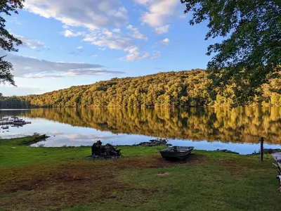 a group of people sitting on the grass near a lake at Catskills Lakefront with Kayaks, HotTub & Firepit in Swan Lake