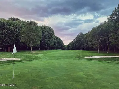 a green golf course with a flag and trees at Designer Poconos Chalet I Ski, Skate, Lakes, Family-Friendly in Lake Ariel