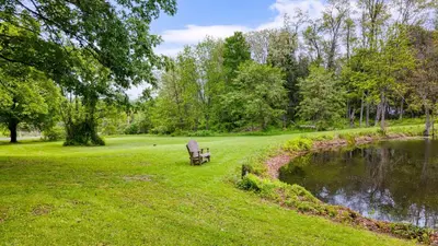 a park bench sitting in the grass next to a pond at Pondfront Gem Minutes from Hudson’s Best Shops Cafes The Stillwater House in Hudson