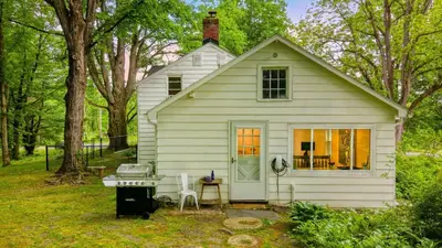 a small white house with a grill in the yard at Pondfront Gem Minutes from Hudson’s Best Shops Cafes The Stillwater House in Hudson
