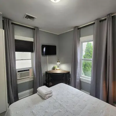a bedroom with a bed and a television and two windows at Bus Train 2 NYC Spacious 4BR SH in South Hackensack