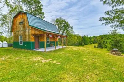 a barn with a green roof on a grass field at Escape to Nature Secluded McDonough Cabin!