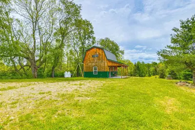 a barn on a grassy field with trees at Escape to Nature Secluded McDonough Cabin!
