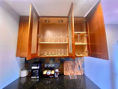 a kitchen with wooden cabinets with glasses on shelves at Easy PATH&Bus access- NYC| designer home + Deck. in Jersey City