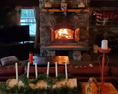 a living room with a stone fireplace with a table and a candle at Serendipity Lake House in Windham