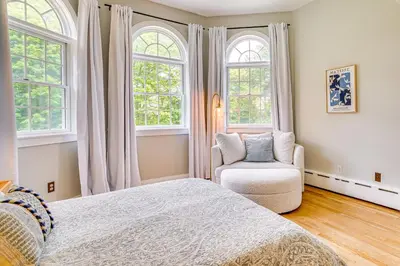 a bedroom with a bed and a chair and windows at Serene Hudson Valley Escape with Pool and Grill in Carmel