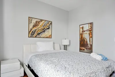 a white bedroom with a bed and two pictures on the wall at 2 Queen Beds, TV's in Bedroom, Path to Manhattan in Jersey City