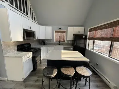 a kitchen with white cabinets and a island with stools at Masthope Retreat in Lackawaxen