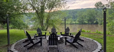 a group of chairs sitting around a fire pit next to a lake at Charming 3-BR Riverside country farmhouse Retreat Huge Yard & Fire Pit