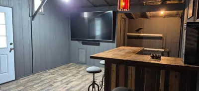 a room with a bar with a large tv on the wall at Charming 3-BR Riverside country farmhouse Retreat Huge Yard & Fire Pit