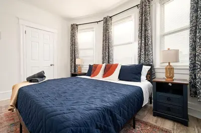 a bedroom with a bed with blue sheets and windows at Whole House Near NYC and Transit with Game Room Fire Pit and King Bed in New Rochelle