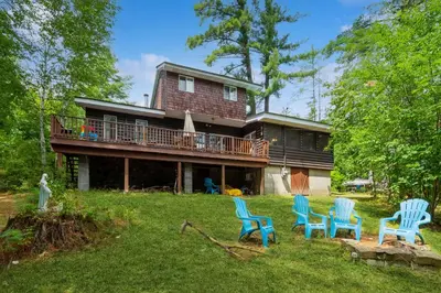 a house with a deck and chairs in the yard at Adirondacks in Style! Lake House with Deck, Fire Pit in Hadley