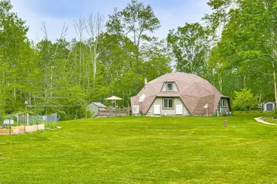 a house with a gambrel roof on a green lawn at Ski, Snowshoe and Fish Dome Escape in Nature! in Warren